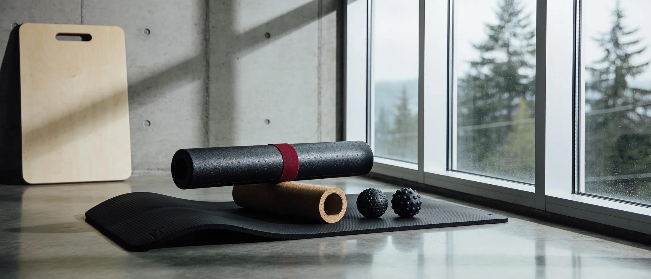 A foam roller, a pair of massage balls and a stretch strap laid out on a cool concrete floor